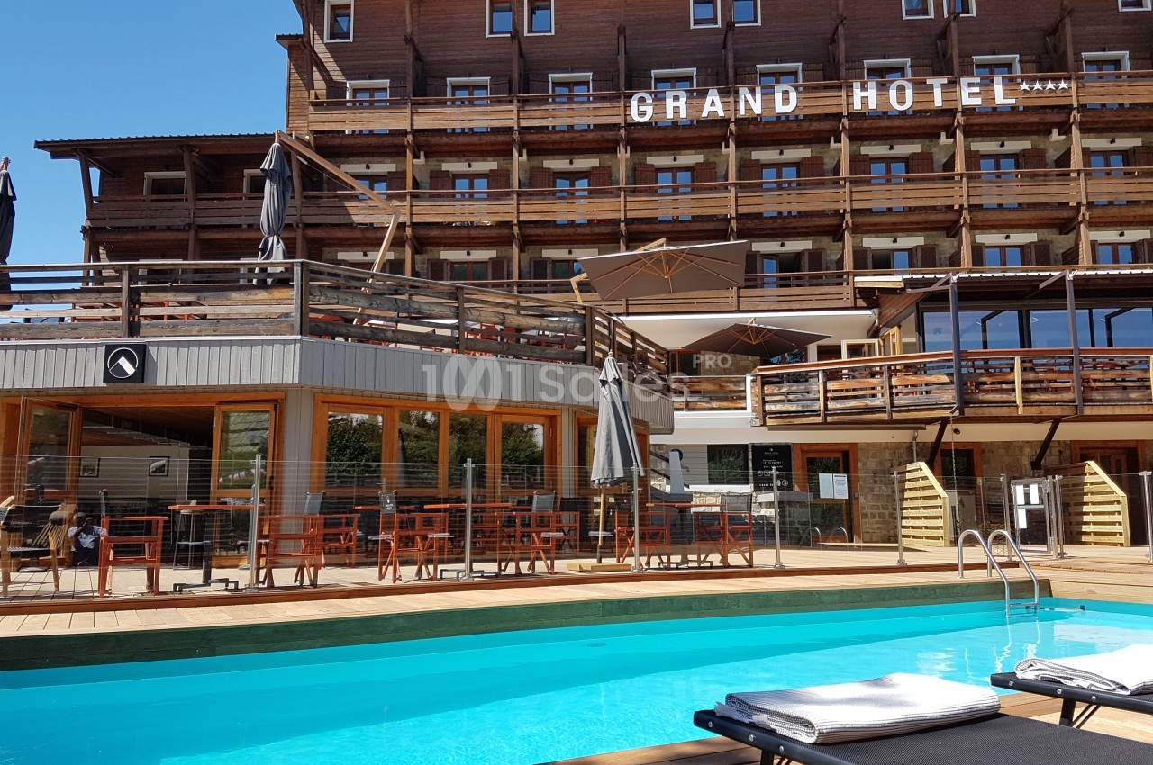 Piscine extérieure avec transats devant un grand hôtel en bois, entourée de terrasses aménagées.