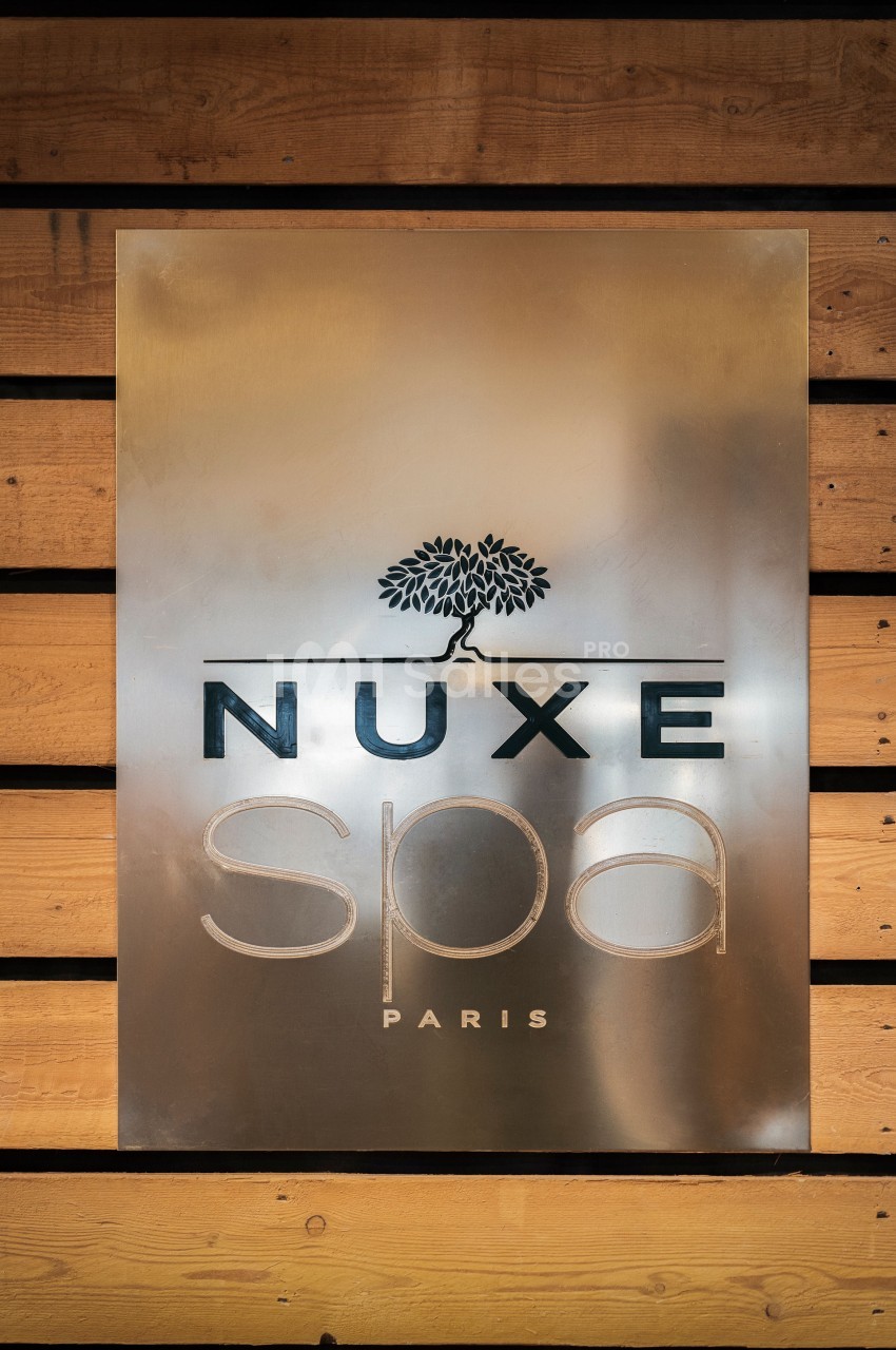 Plaque métallique avec le logo ’Nuxe Spa Paris’ gravé, fixée sur un mur en bois.
