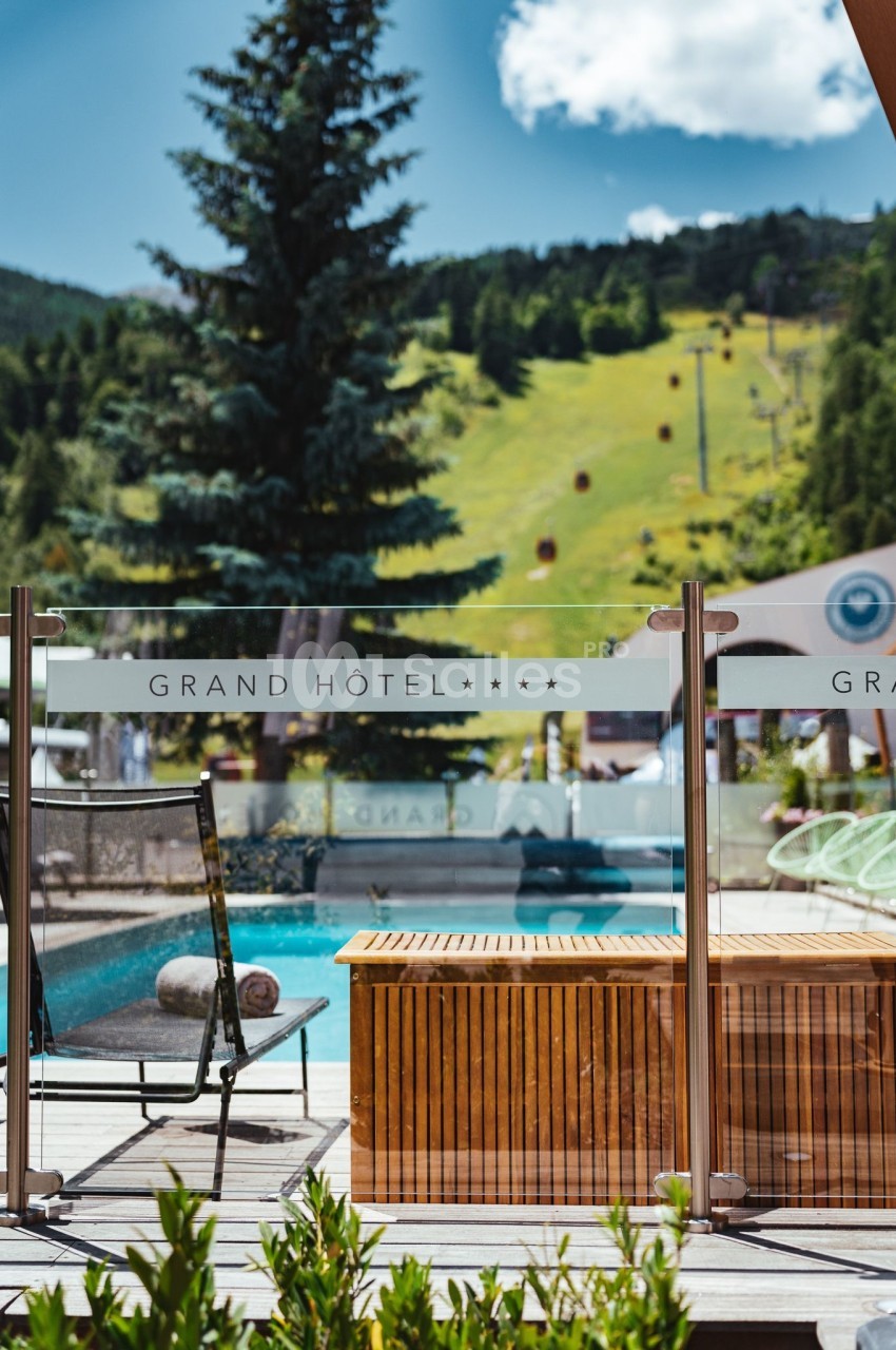 Vue d'une terrasse avec piscine, transat et montagne verdoyante en arrière-plan, devant un panneau ’Grand Hôtel’.