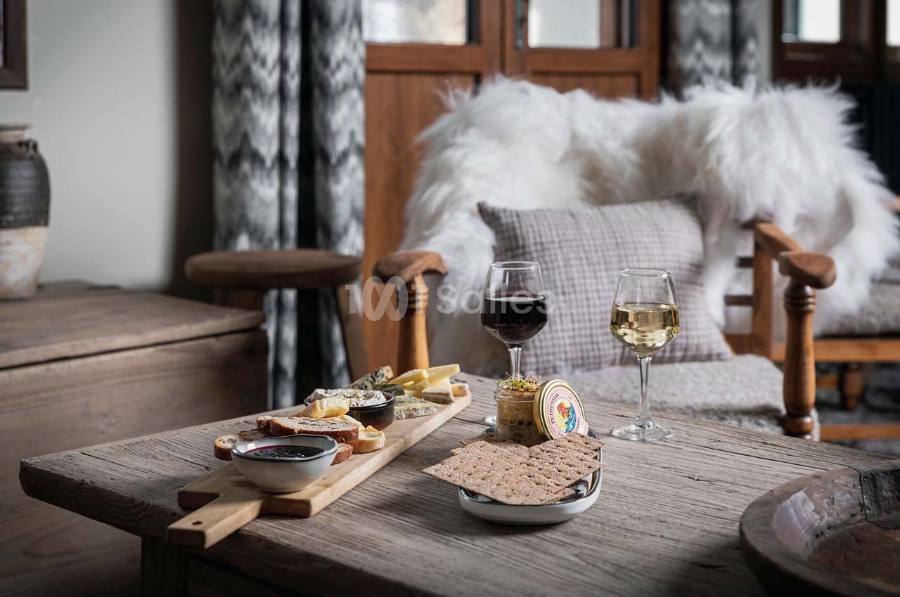 Plateau de fromages et charcuteries avec deux verres de vin sur une table en bois dans un salon cosy.