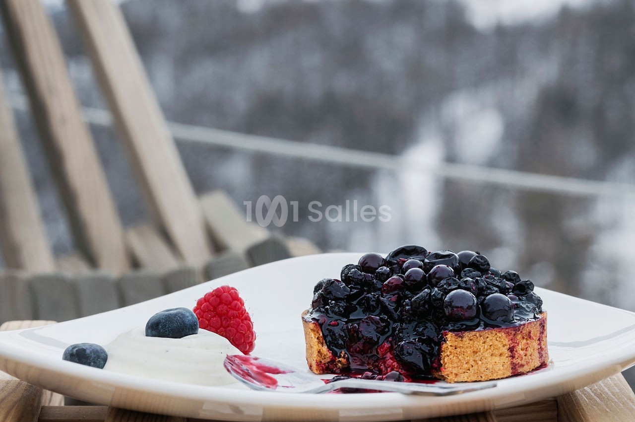 Un dessert composé d'un gâteau aux fruits rouges, accompagné de crème et de baies, présenté sur une terrasse en hiver.