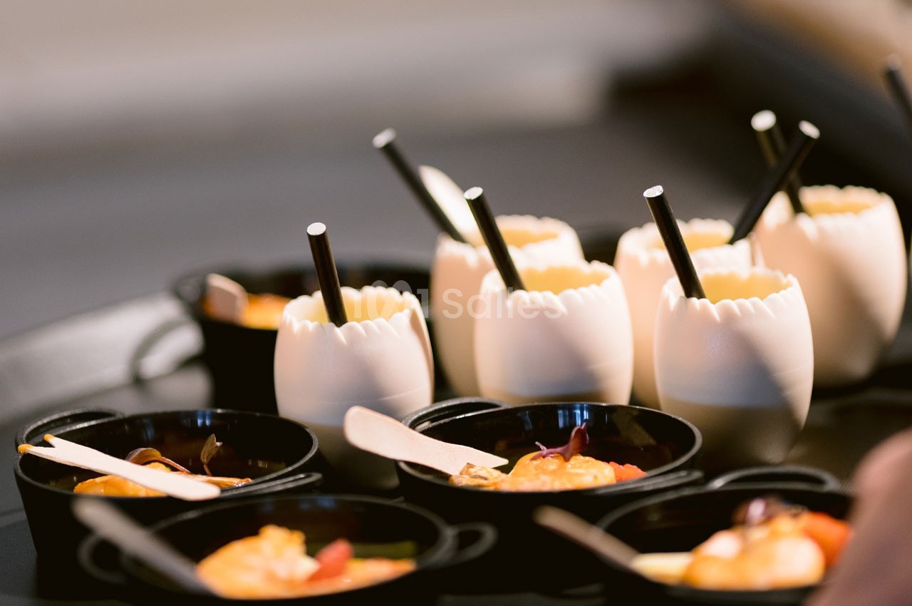 Des verrines en coquilles d'œufs et des mini-casseroles noires contenant des préparations culinaires sur un plateau.