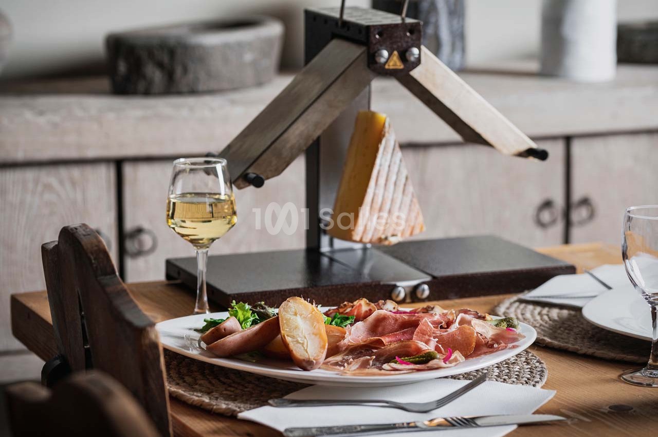 Assiette de raclette avec charcuterie, pommes de terre et salade, servie à côté d'un appareil à raclette et d'un verre de…