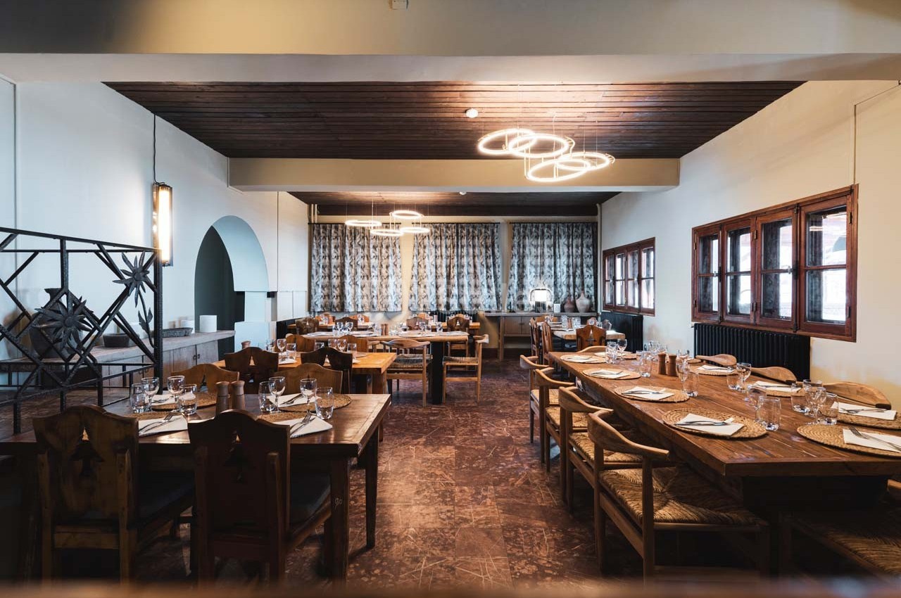 Salle de restaurant lumineuse avec tables en bois dressées, grandes fenêtres et décor sobre.
