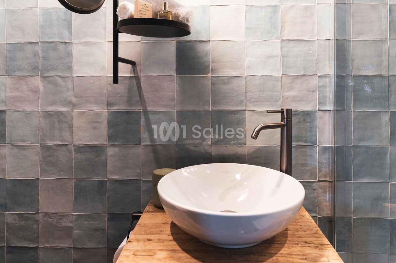 Lavabo blanc posé sur un meuble en bois, avec un robinet métallique et un mur de carreaux bleus en arrière-plan.