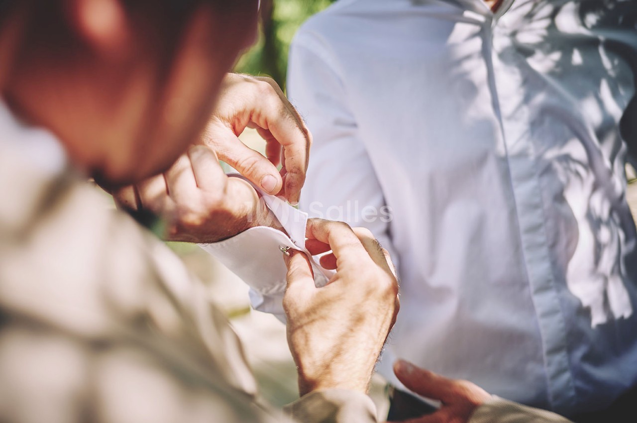 Une personne ajuste le bouton de manchette d'une chemise blanche portée par une autre personne en extérieur.