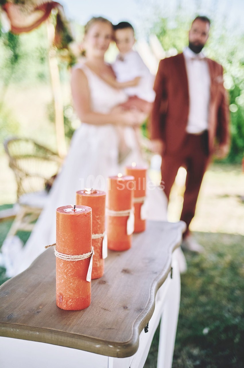 Quatre bougies rouges décoratives posées sur une table en bois, avec un couple et un enfant flous en arrière-plan.