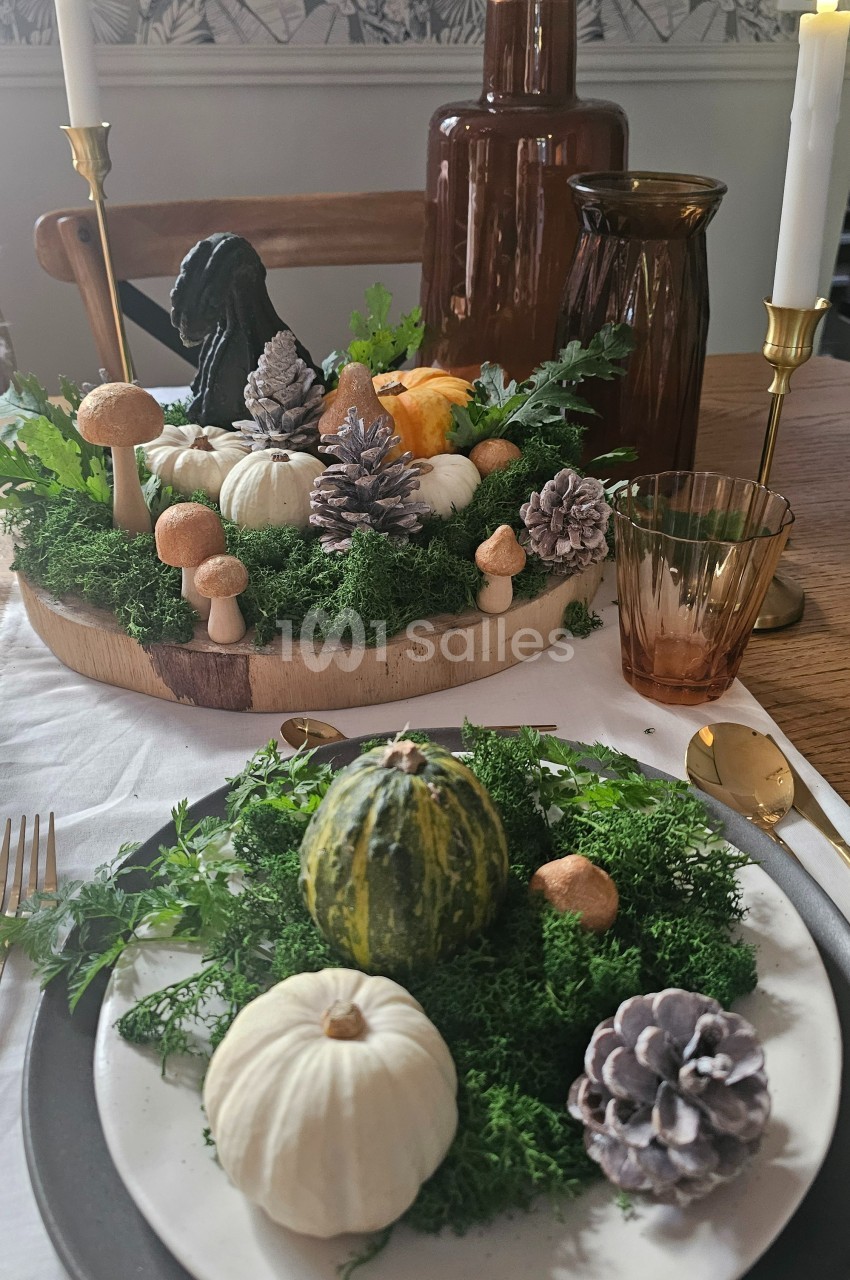 Décoration de table automnale avec citrouilles, mousse, pommes de pin et bougies dans une ambiance chaleureuse.