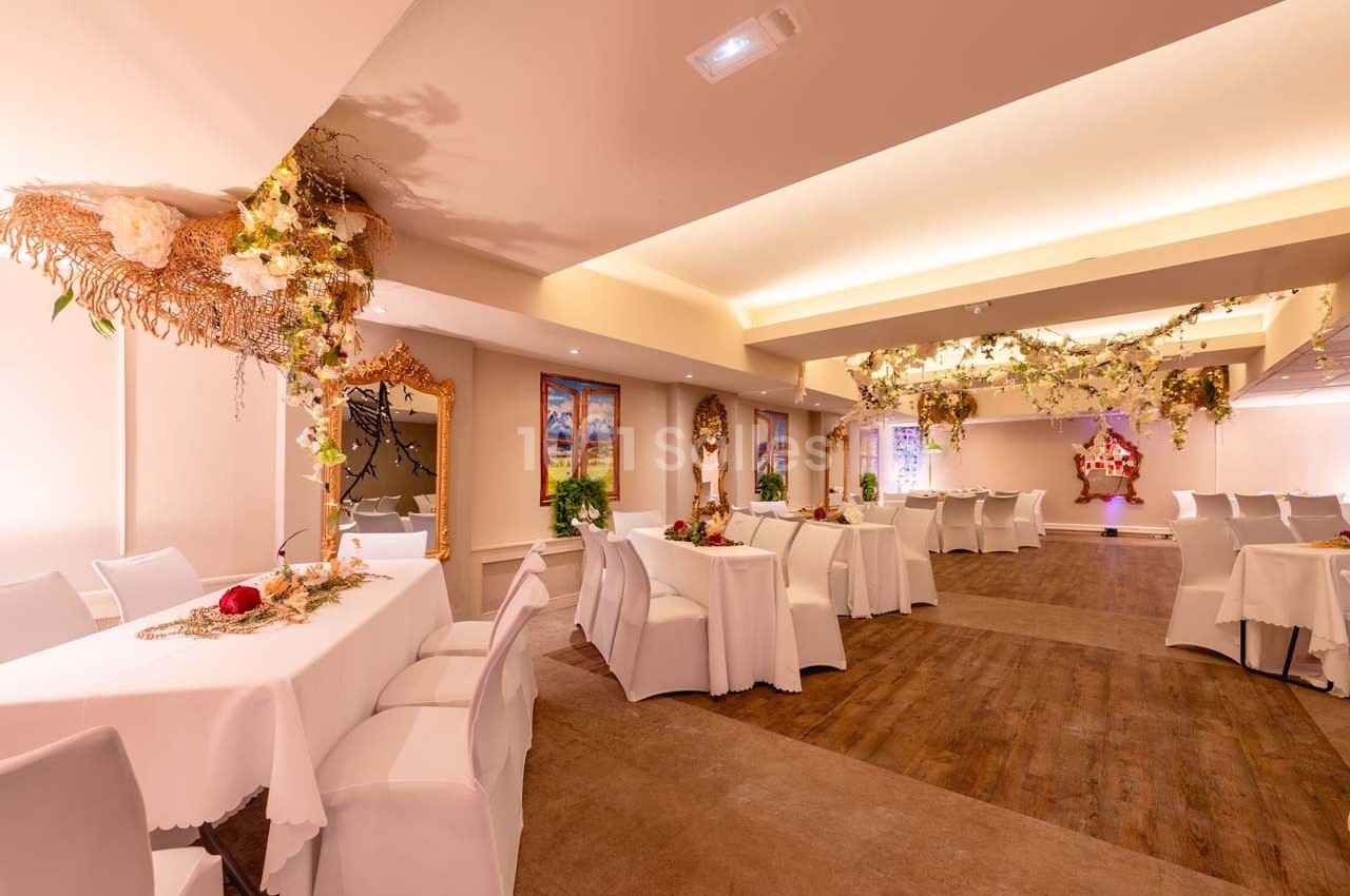 Salle de réception décorée avec des tables blanches, des chaises assorties et des ornements floraux suspendus.
