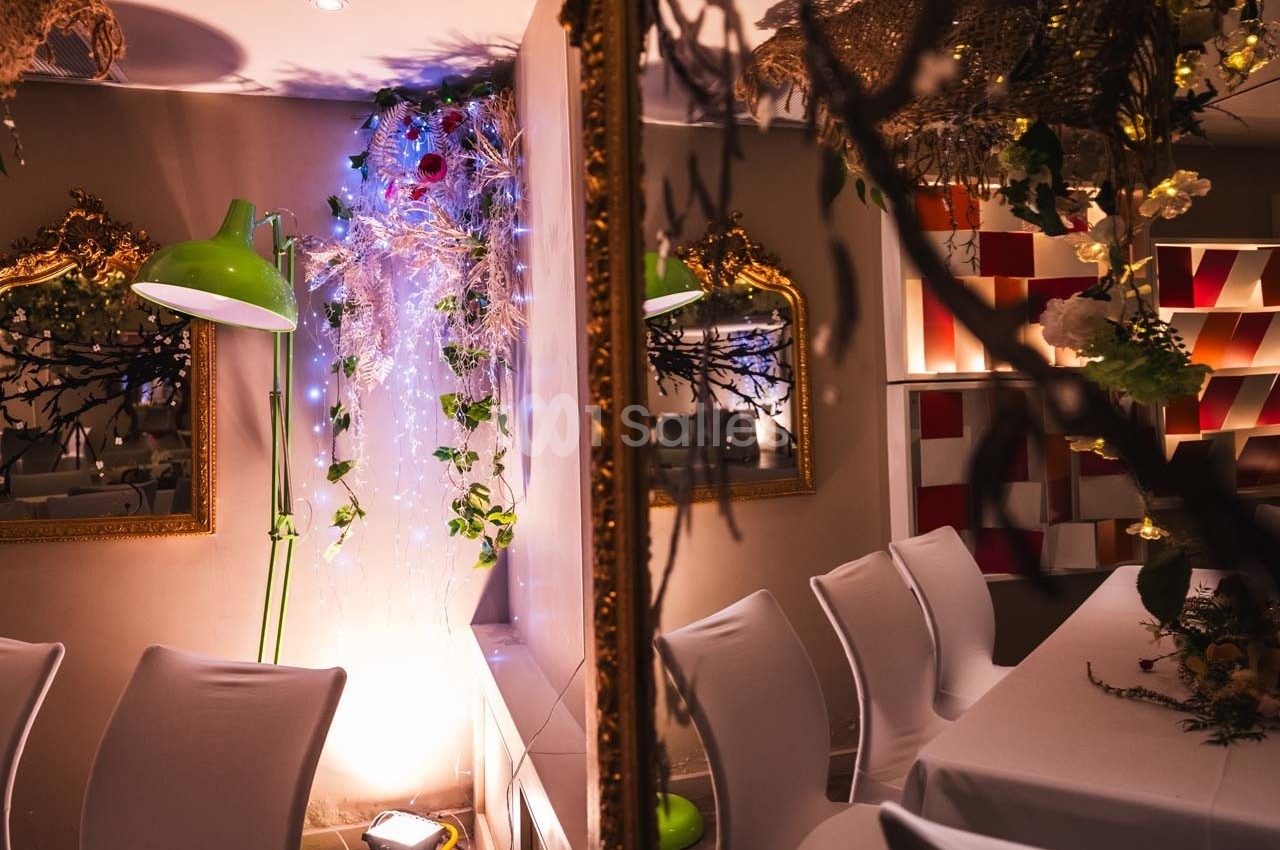 Salle décorée avec des chaises blanches, un miroir doré, une lampe verte et des guirlandes lumineuses.