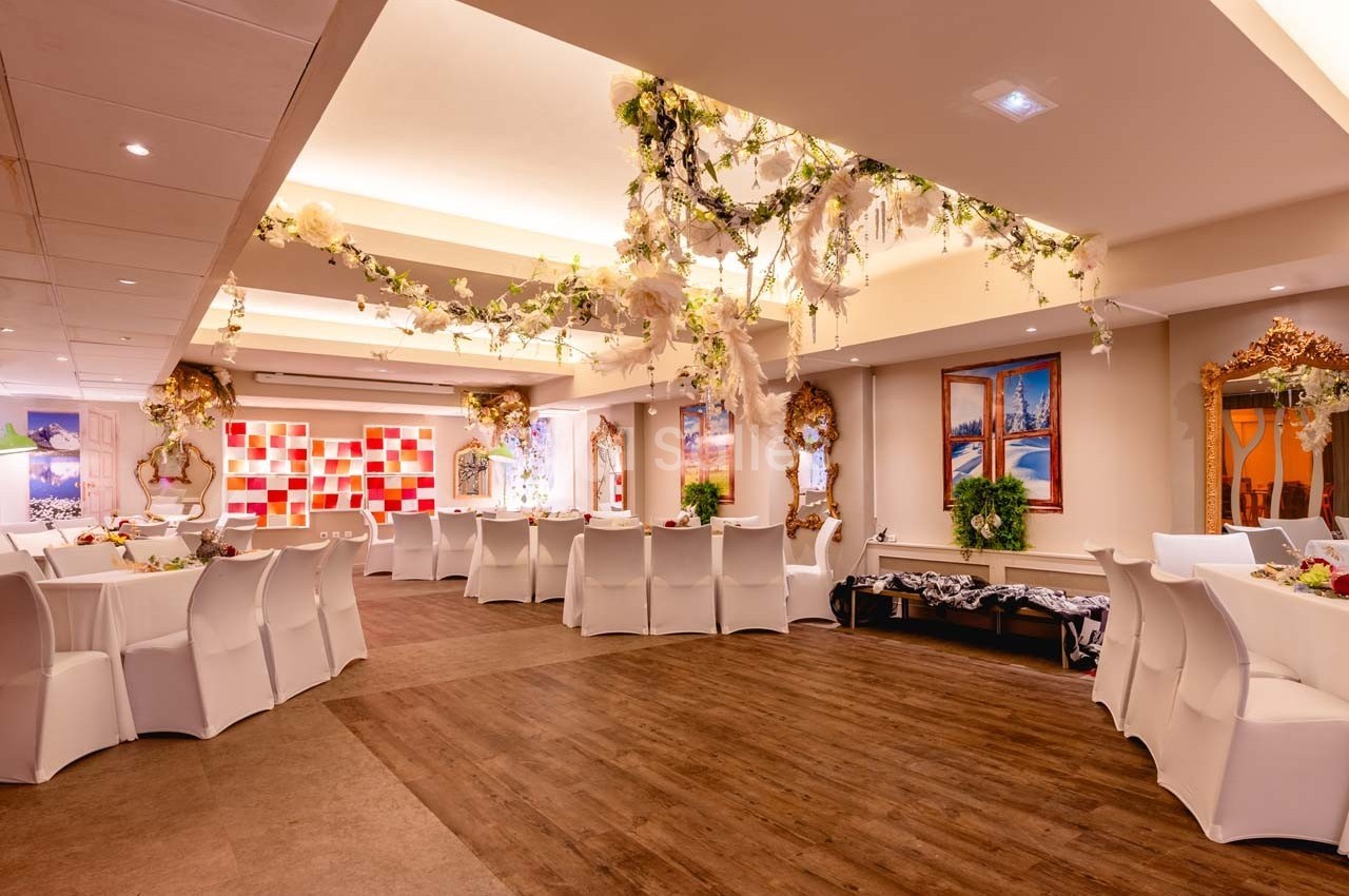 Salle de réception décorée avec des fleurs suspendues, des tables rondes dressées et un sol en bois.