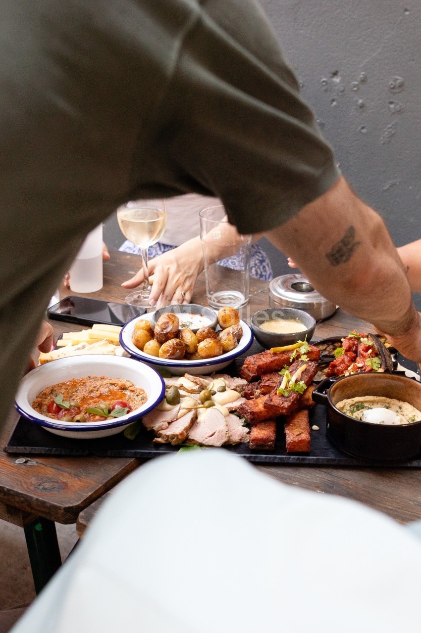 Un groupe partage un repas composé de viande, pommes de terre et accompagnements sur une table en extérieur.