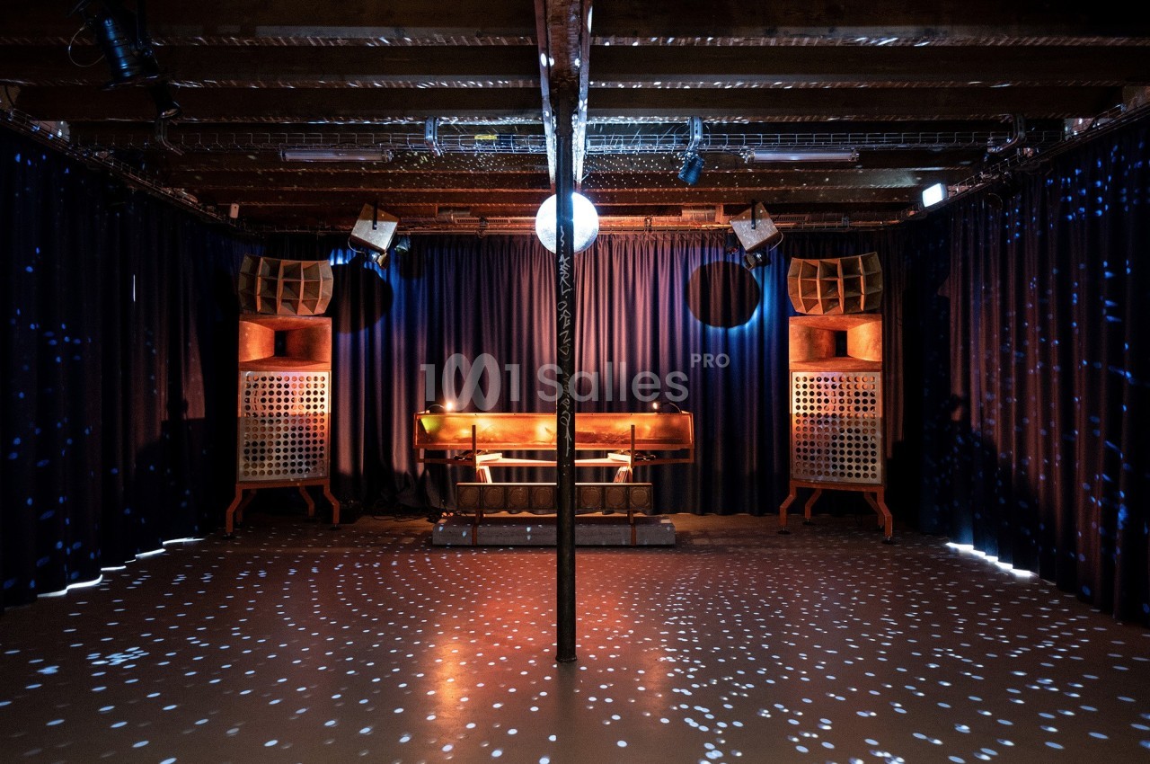 Salle sombre avec une piste de danse éclairée par une boule disco, entourée de rideaux et d'enceintes en bois.