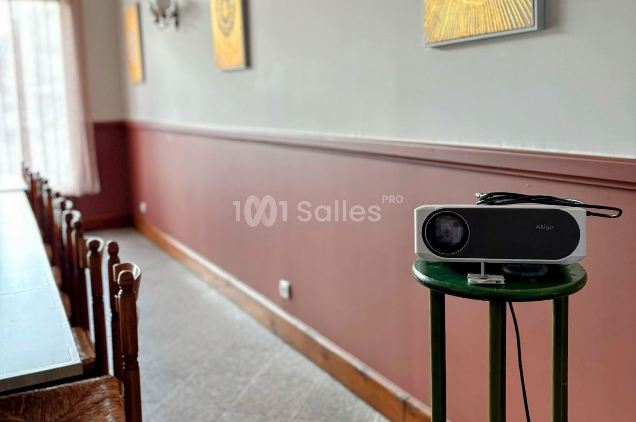 Projecteur posé sur un tabouret vert dans une pièce avec des murs bicolores et des tableaux accrochés.