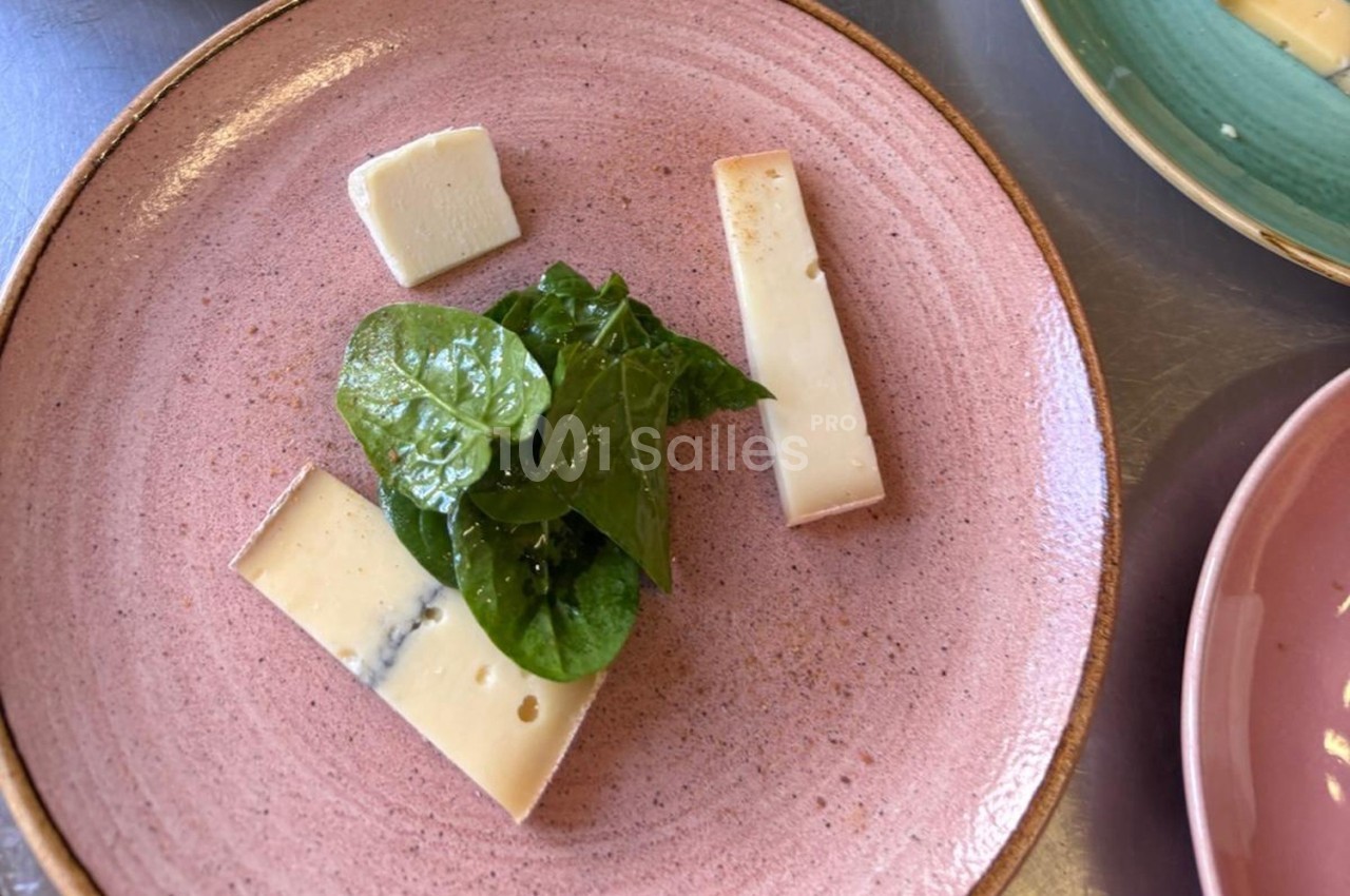 Assiette rose contenant des morceaux de fromage et des feuilles de salade verte.