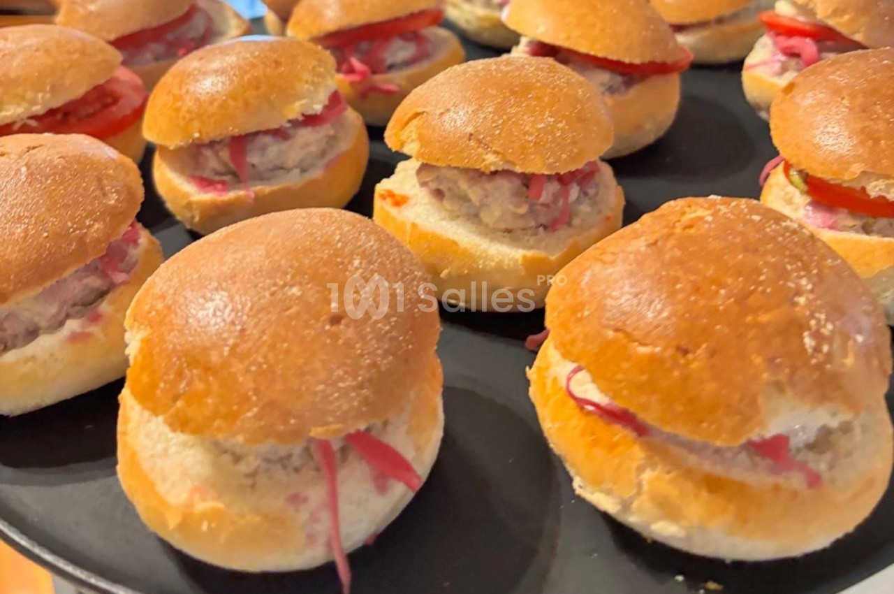 Petits burgers garnis de viande hachée et légumes, disposés sur un plateau noir.