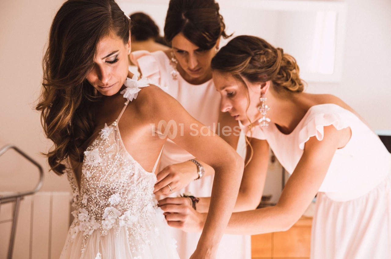 Deux femmes ajustent la robe de mariée d'une troisième femme dans une pièce lumineuse.