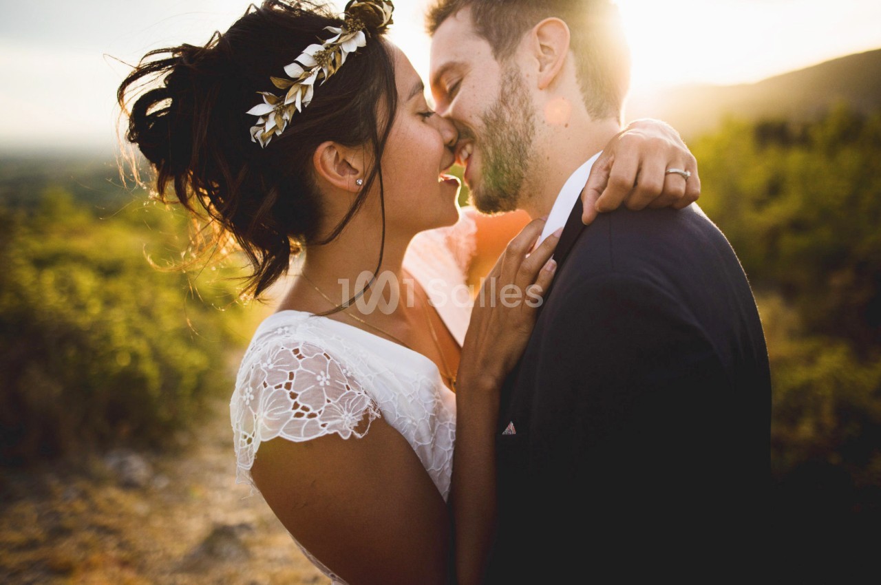 Un couple en tenue de mariage s'embrasse tendrement en extérieur au coucher du soleil.