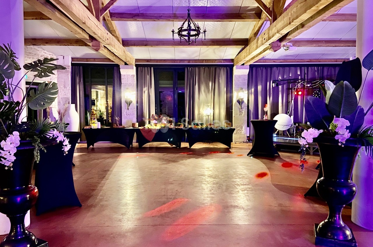 Salle de réception décorée avec des plantes, des tables drapées de noir et un éclairage tamisé coloré.
