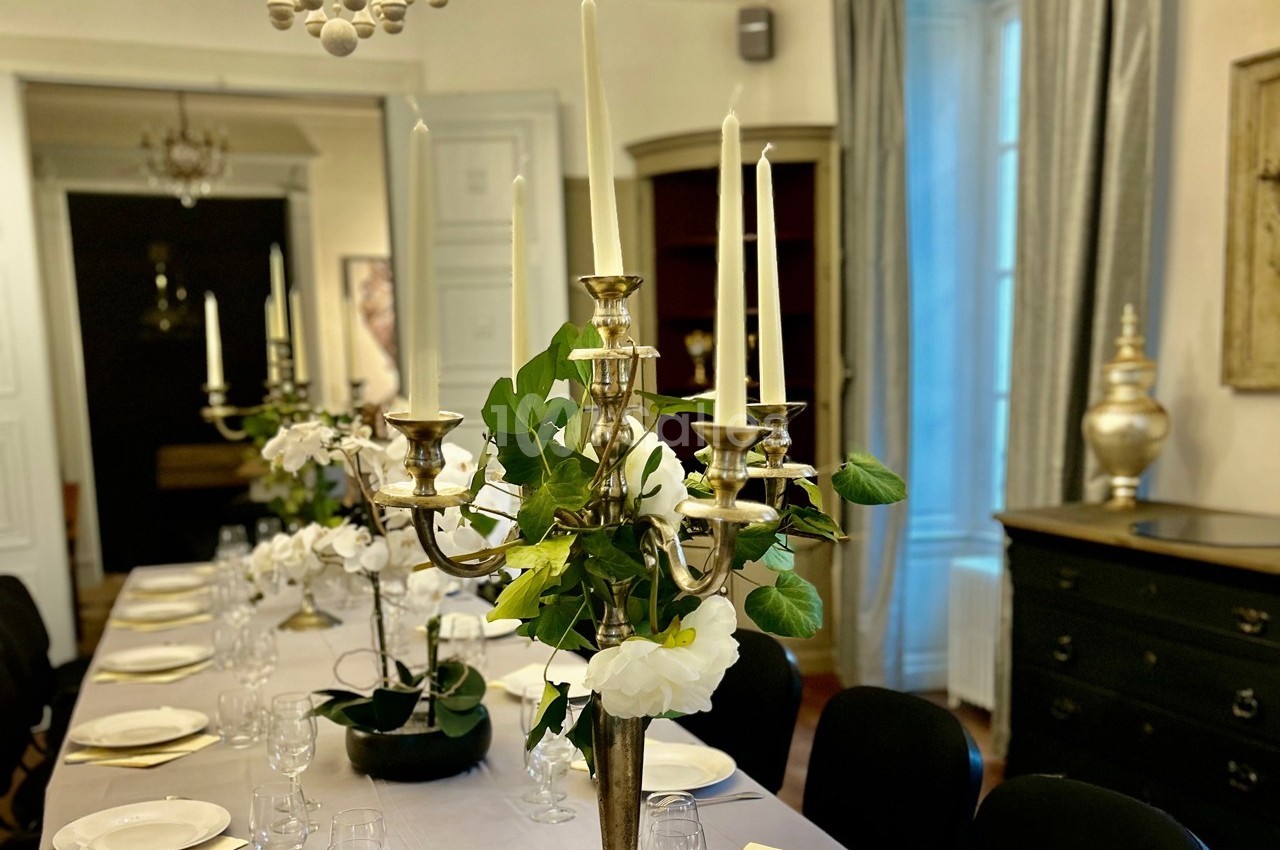 Table élégamment dressée avec chandeliers dorés, fleurs blanches et vaisselle, dans une salle lumineuse et raffinée.