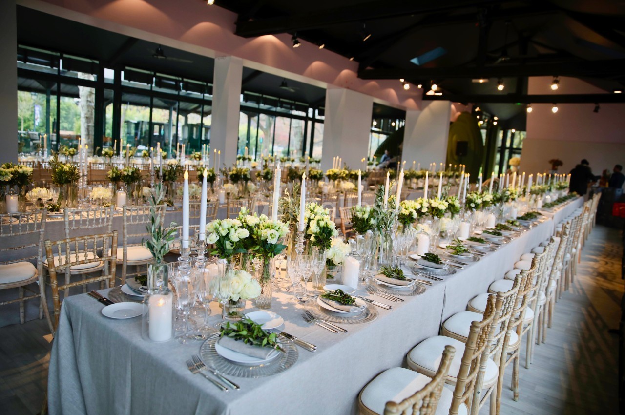 Salle de réception décorée avec des tables élégantes, chandeliers, fleurs blanches et chaises en bois clair.