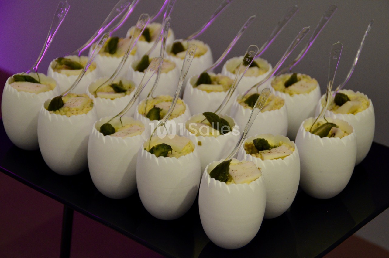 Des verrines en forme de coquilles d'œufs contenant une préparation garnie de feuilles vertes, servies avec des cuillères…