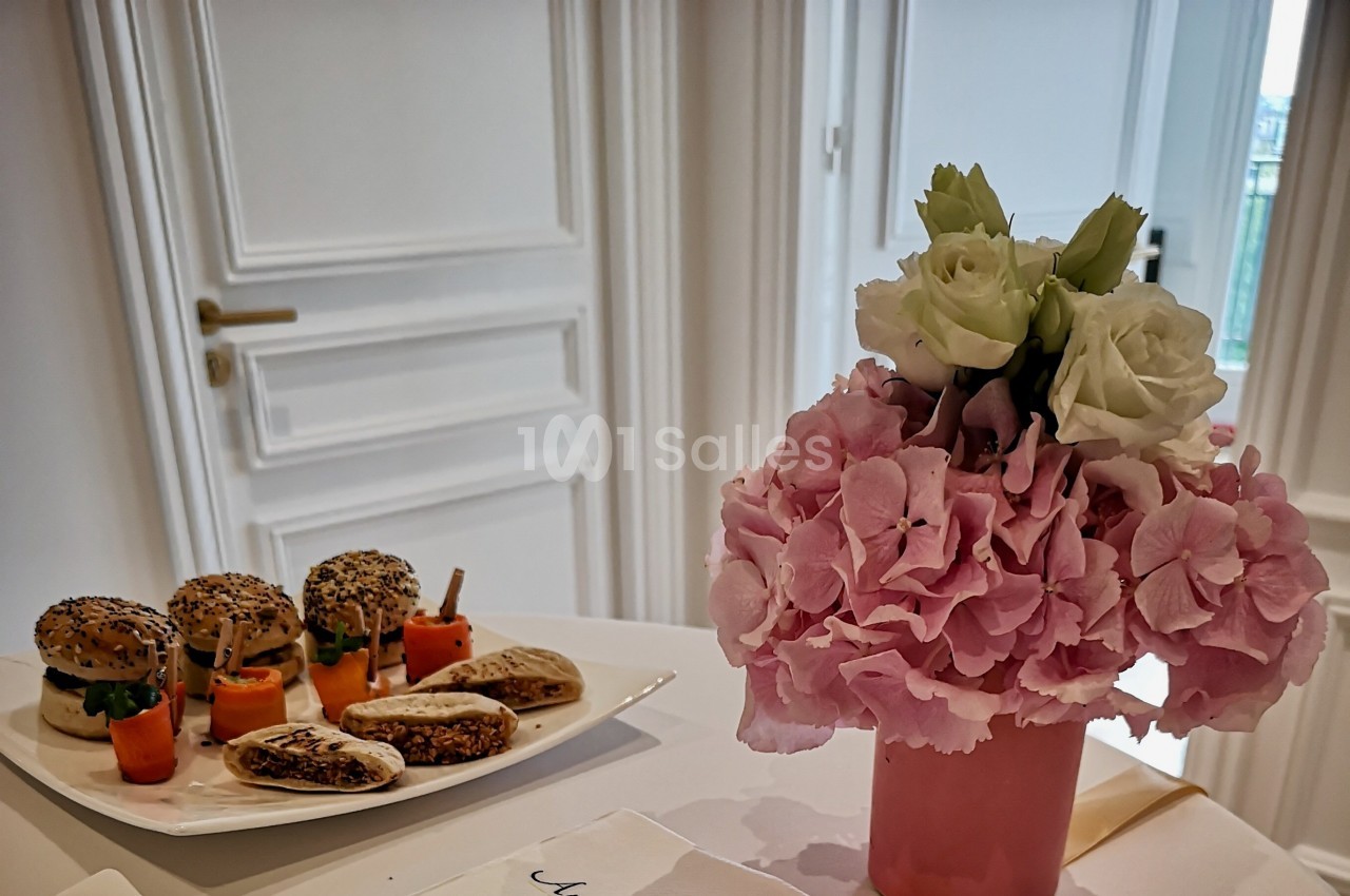 Assiette de mini-sandwichs et légumes en apéritif sur une table, avec un bouquet de fleurs roses et blanches au premier plan.