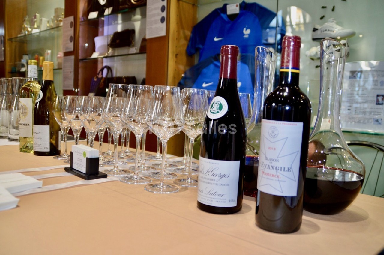 Bouteilles de vin rouge et blanc avec verres à vin alignés sur une table, devant une vitrine d'objets divers.