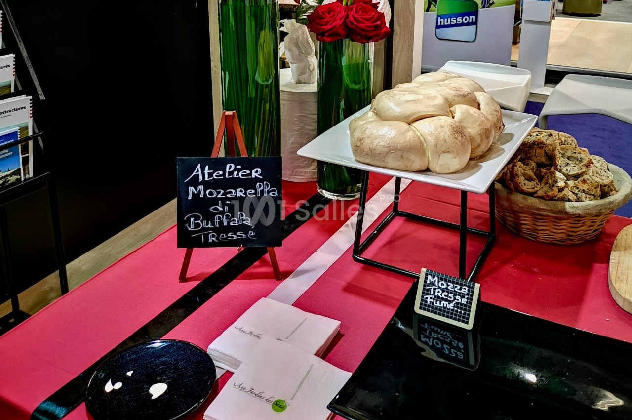 Plateau de mozzarella tressée sur une table rouge, accompagné de pain tranché et d'une ardoise indiquant ’Atelier Mozzarella…