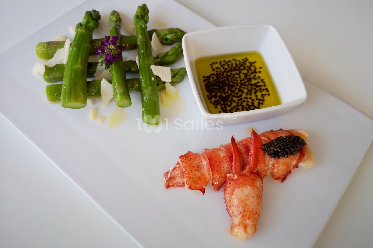 Assiette composée d'asperges vertes avec copeaux de parmesan, homard, caviar et une sauce à l'huile d'olive.