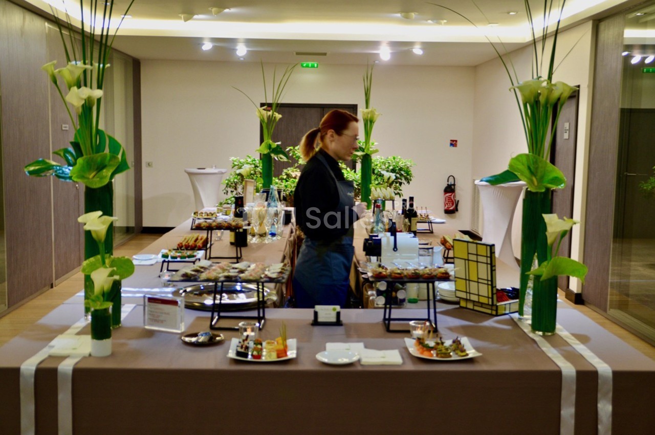 Table de buffet élégamment dressée avec divers plats et boissons, décorée de fleurs blanches, dans une salle lumineuse.