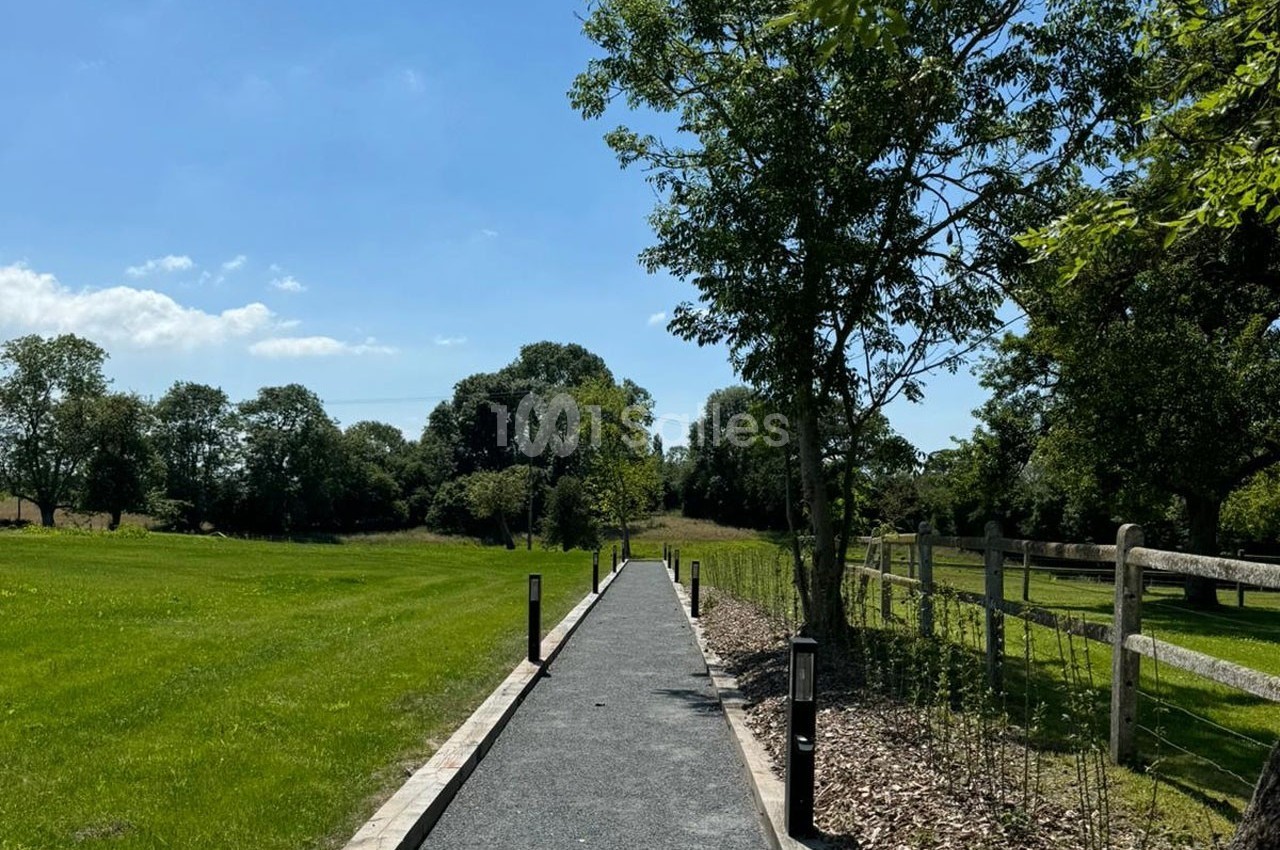 Chemin pavé bordé d'herbe, d'arbres et d'une clôture en bois, sous un ciel bleu dégagé.