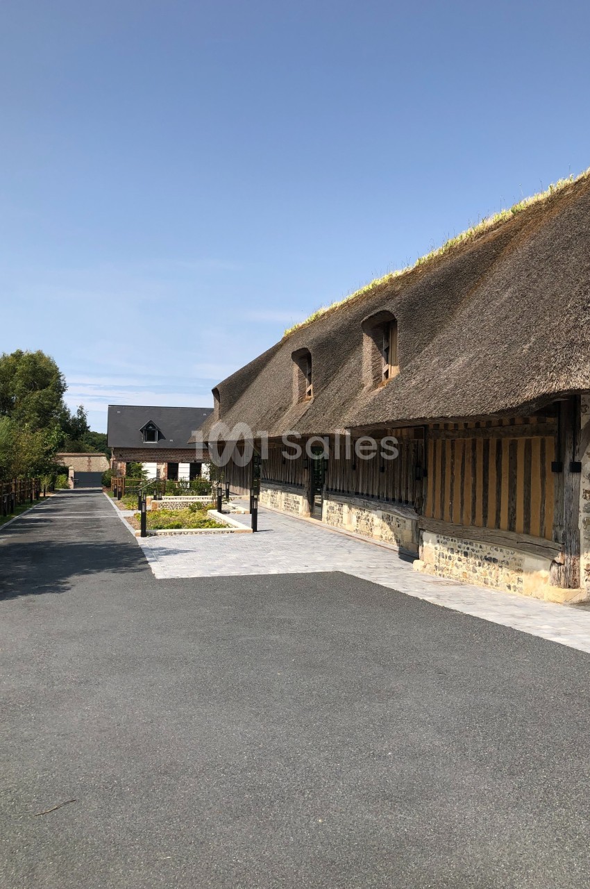 Bâtiment traditionnel à toit de chaume avec façade en colombages, bordé d'une allée pavée et d'espaces verts.