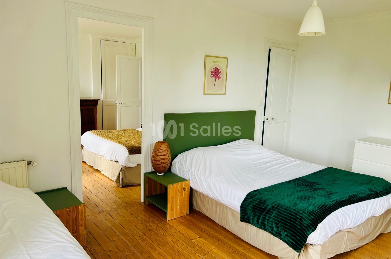 Chambre lumineuse avec parquet, deux lits simples, linge de lit blanc et décoration minimaliste.