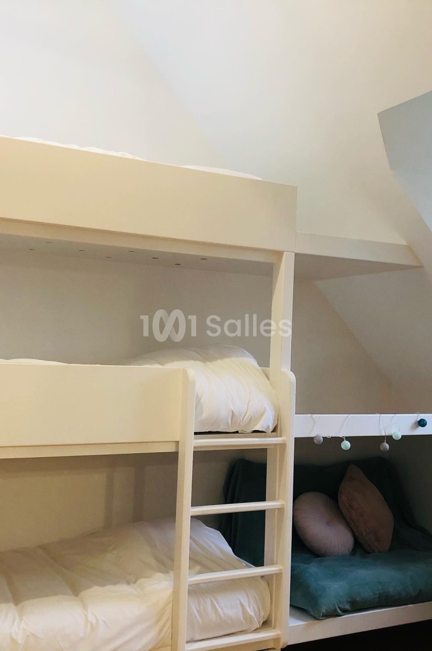 Lit superposé blanc avec échelle, accompagné d'une alcôve aménagée avec coussins et guirlande lumineuse.