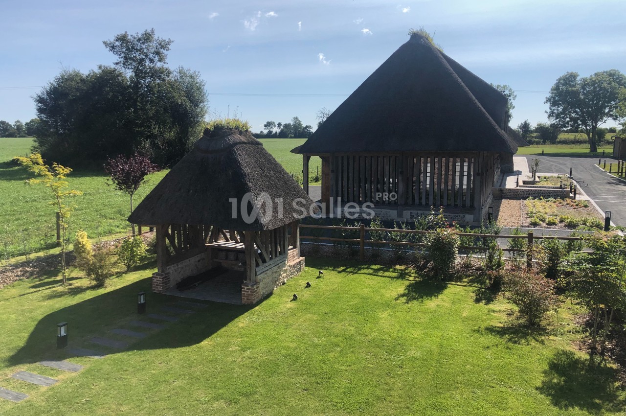 Deux pavillons en toit de chaume entourés de pelouses et jardins, situés dans un paysage rural ensoleillé.