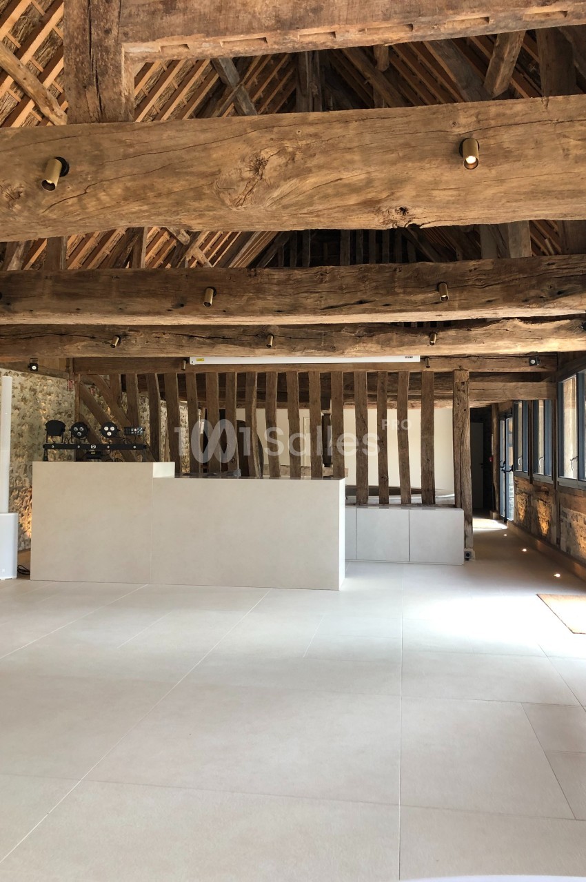 Intérieur d'une salle rénovée avec poutres en bois apparentes, murs en pierre et comptoir moderne au centre.