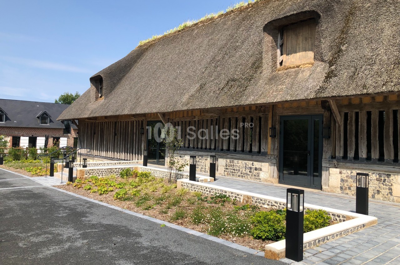 Bâtiment traditionnel à toit de chaume avec façade en bois et pierre, entouré d'un jardin aménagé.