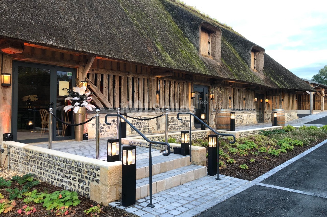 Façade d'un bâtiment ancien à toit de chaume, avec entrée éclairée et décorations florales sur les marches.