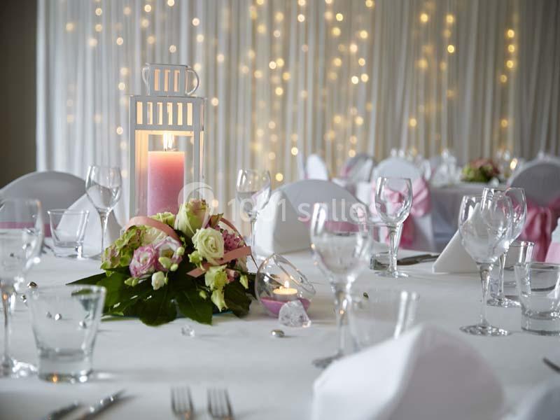 Table décorée pour un mariage avec bougie, fleurs roses et blanches, verres et nappes blanches, fond lumineux.