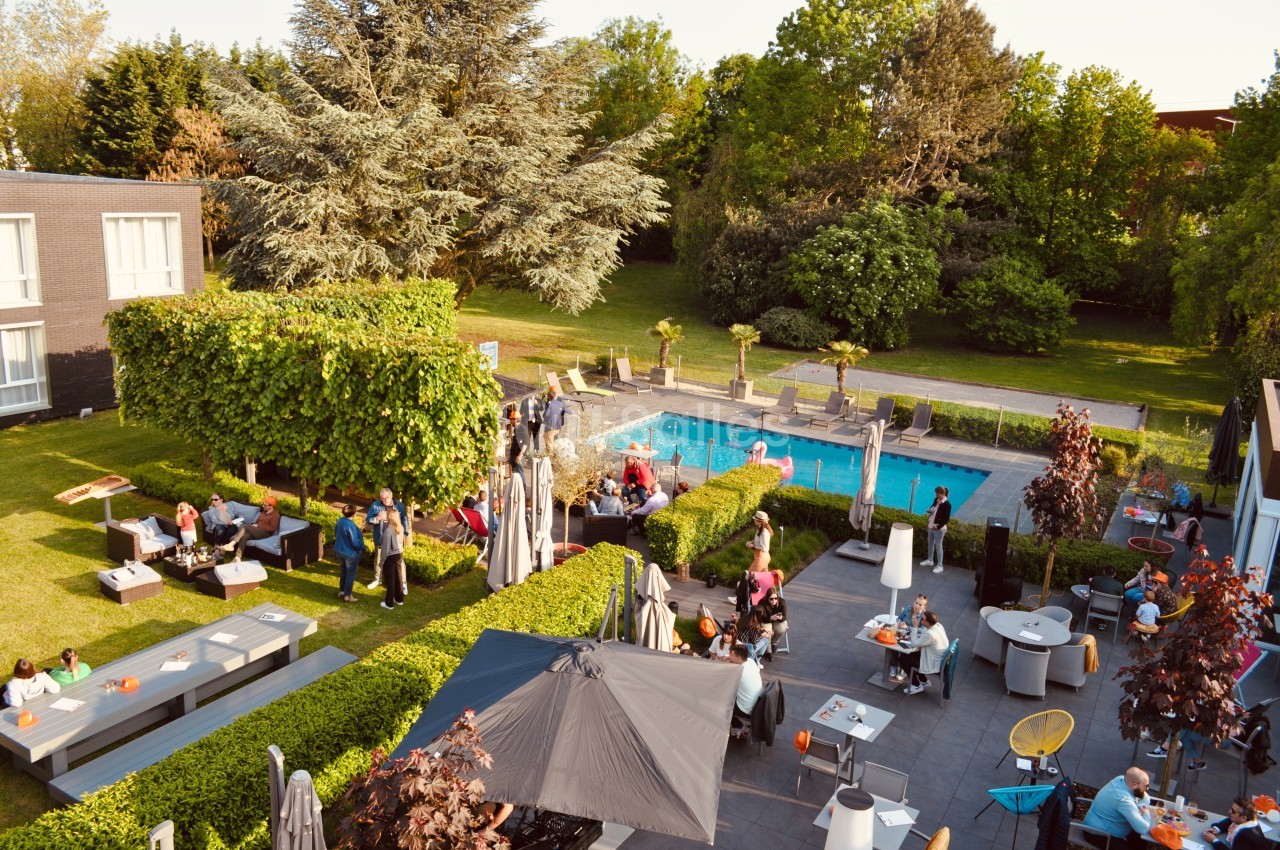 Vue aérienne d'une terrasse animée avec des tables, des parasols et une piscine entourée de verdure.