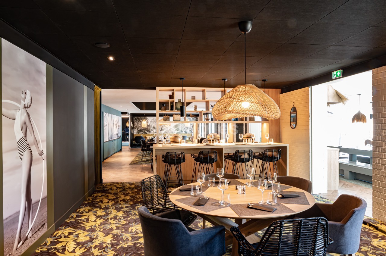 Salle de restaurant moderne avec table ronde dressée, bar en arrière-plan et décoration contemporaine.