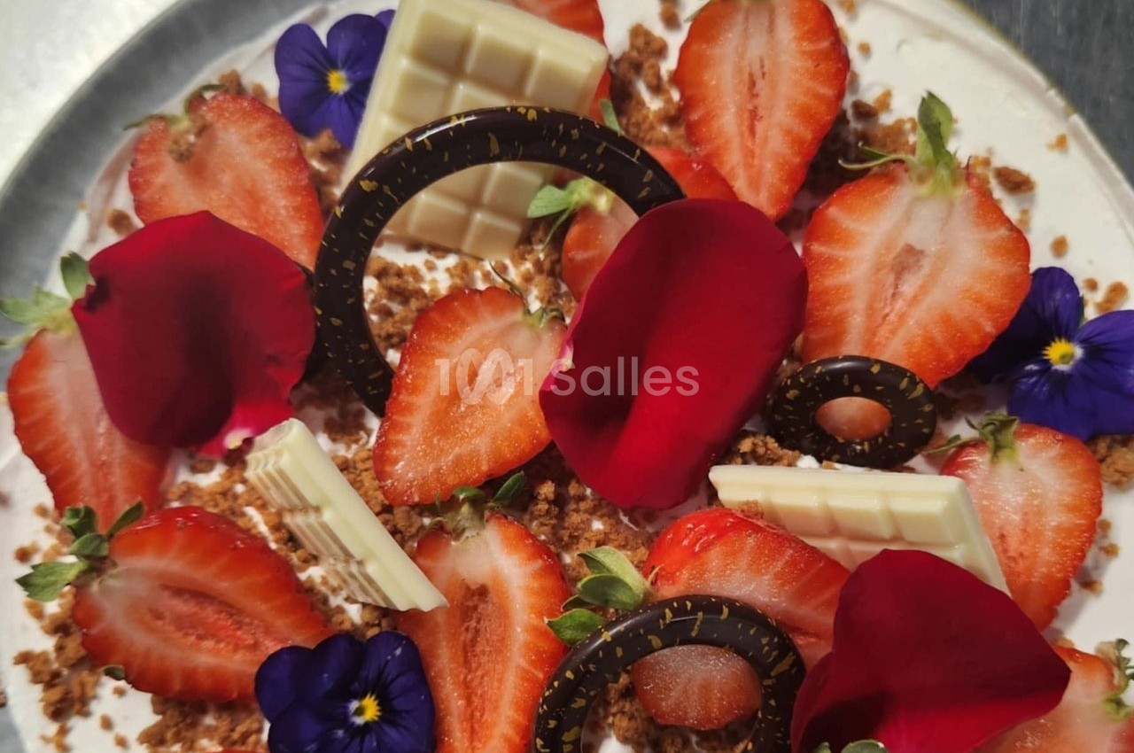 Dessert décoré de fraises, pétales rouges, fleurs comestibles, chocolat blanc et noir sur une base crémeuse.