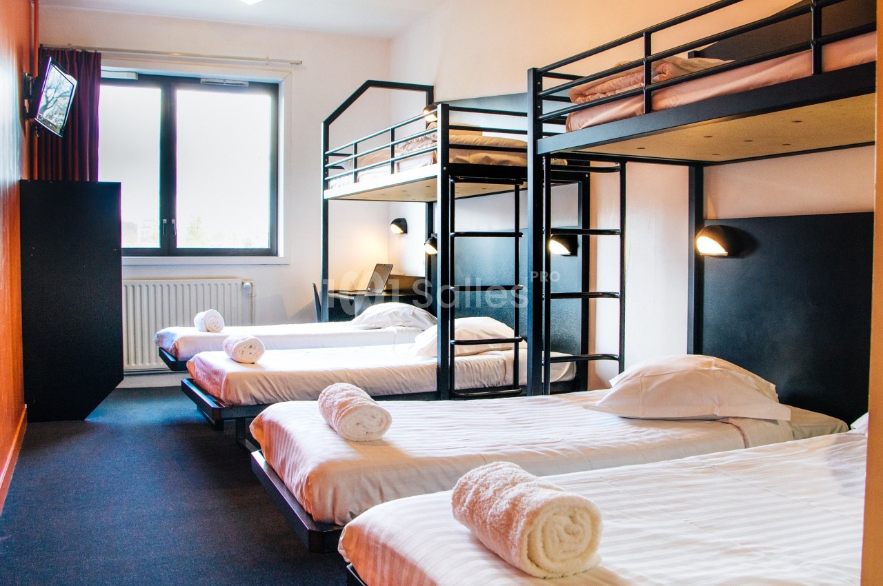 Chambre avec lits superposés et lits simples, éclairage mural, fenêtre lumineuse et télévision fixée au mur.