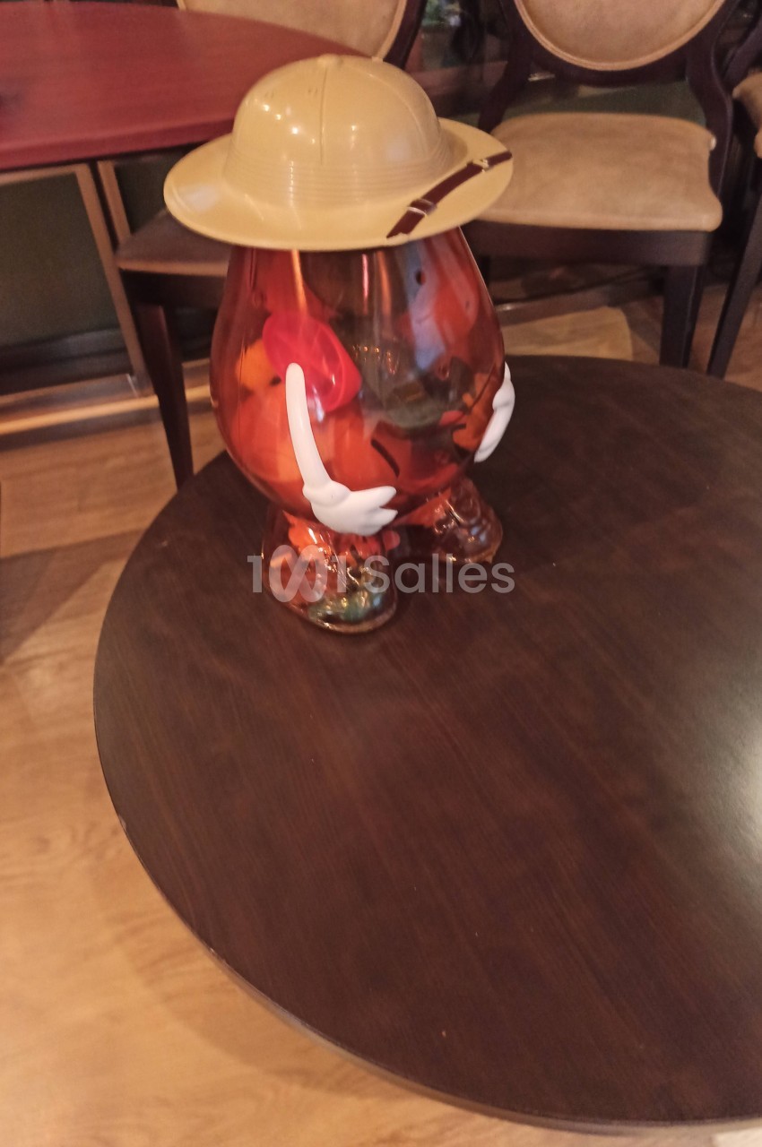 Figurine en plastique translucide en forme de patate, portant un chapeau beige, posée sur une table en bois.