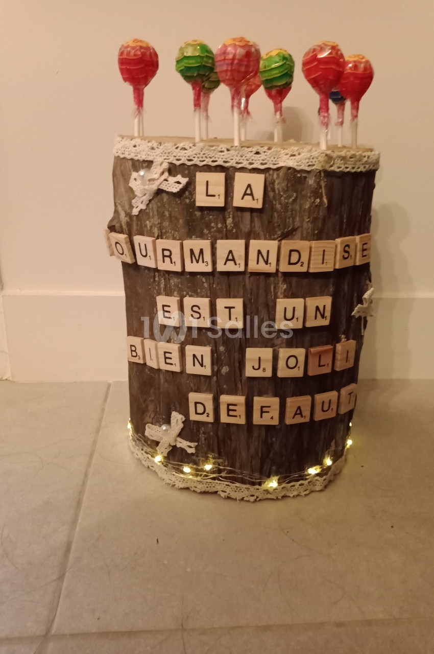 Bûche décorative ornée de lettres en bois formant une phrase et de sucettes colorées plantées sur le dessus.