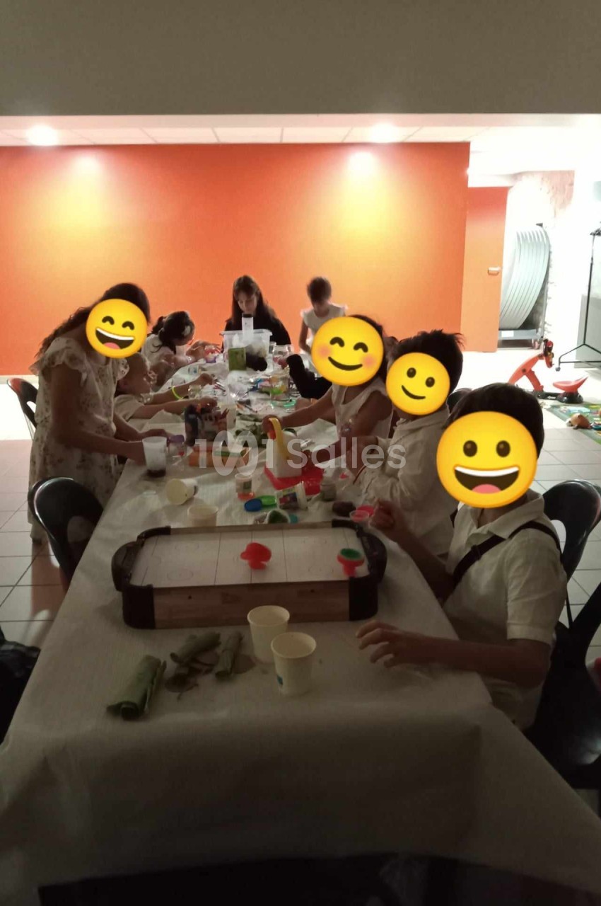 Des personnes assises autour d'une table participent à une activité manuelle dans une salle éclairée.