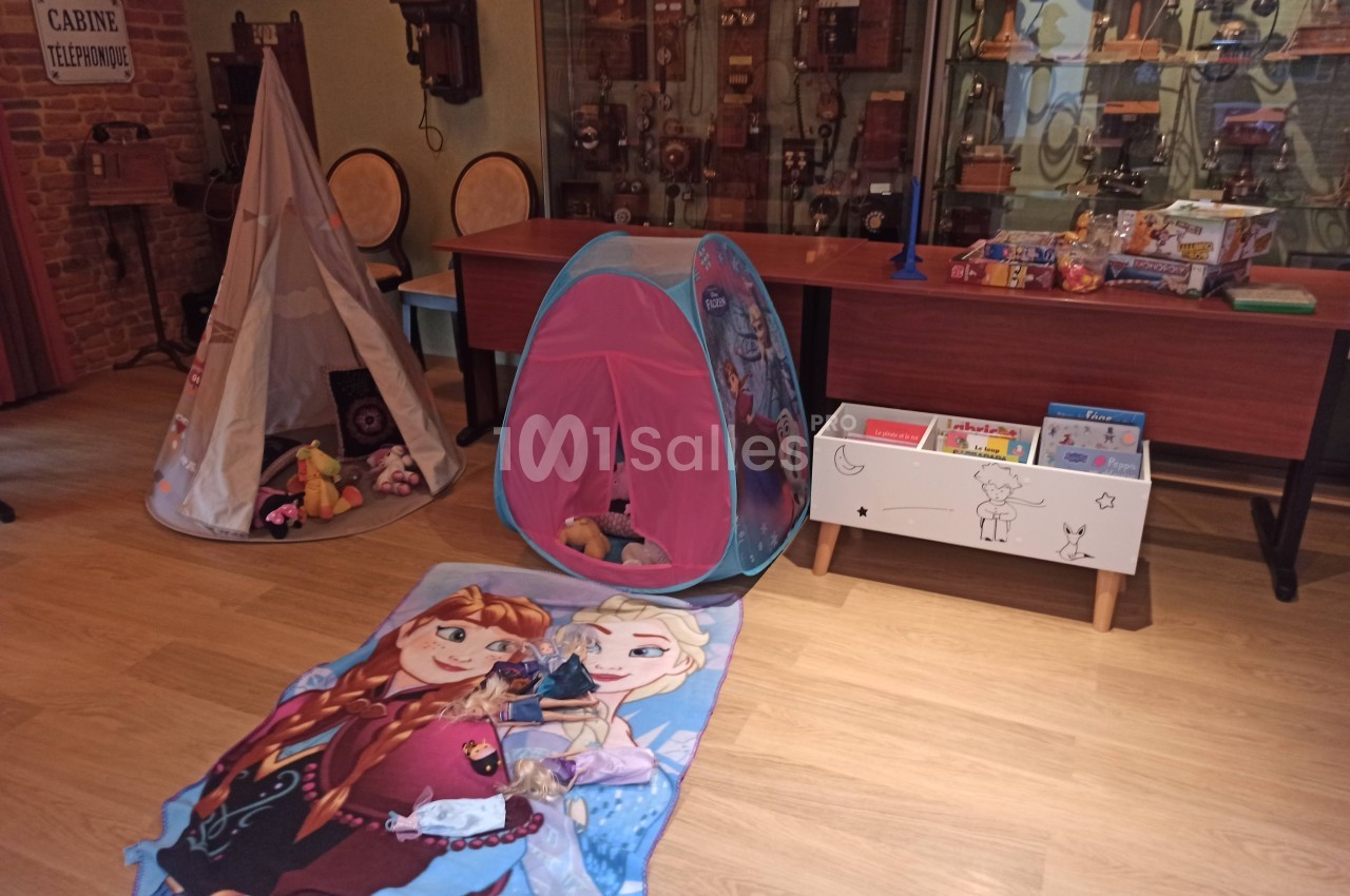 Espace de jeu pour enfants avec tentes, jouets, tapis décoré et meubles en bois dans une pièce au style rétro.