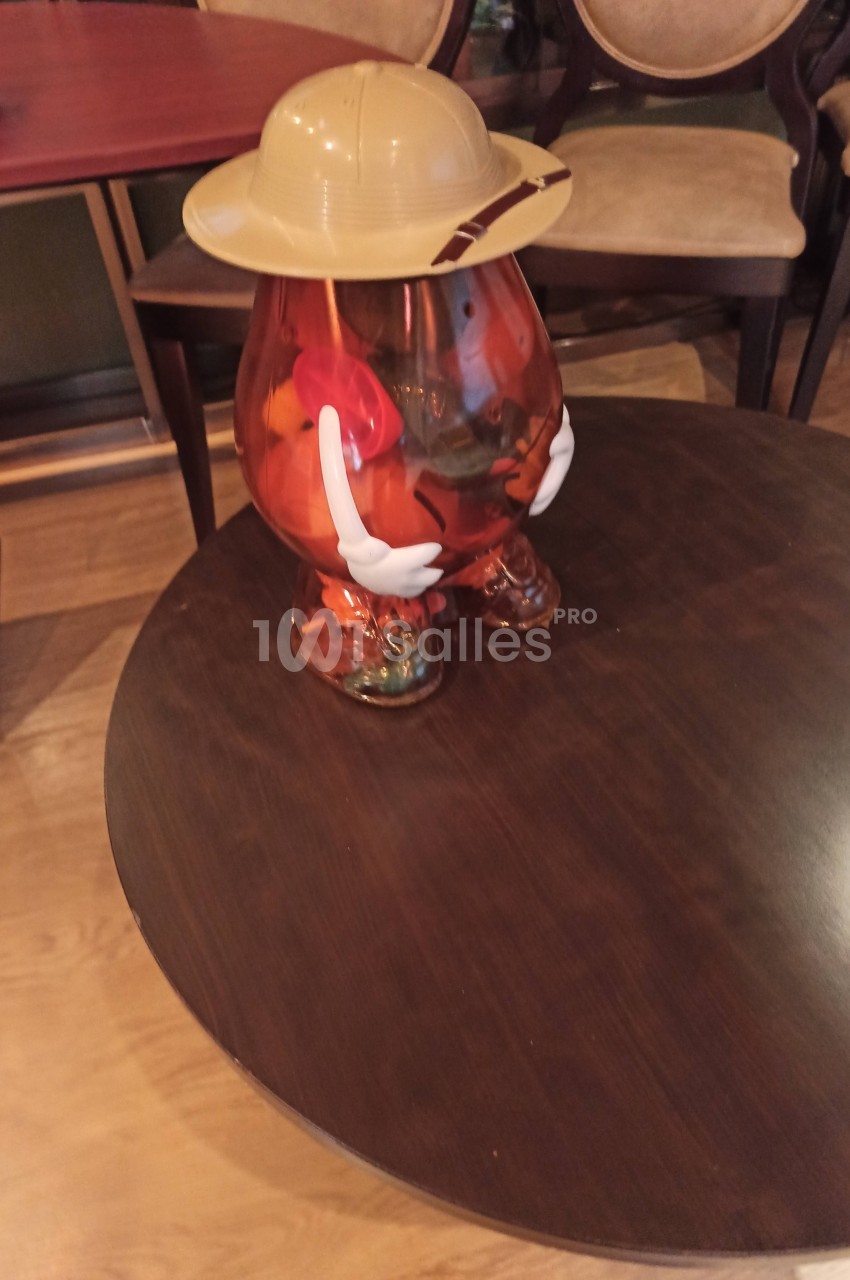 Figurine en plastique translucide en forme de patate, portant un chapeau beige, posée sur une table en bois.