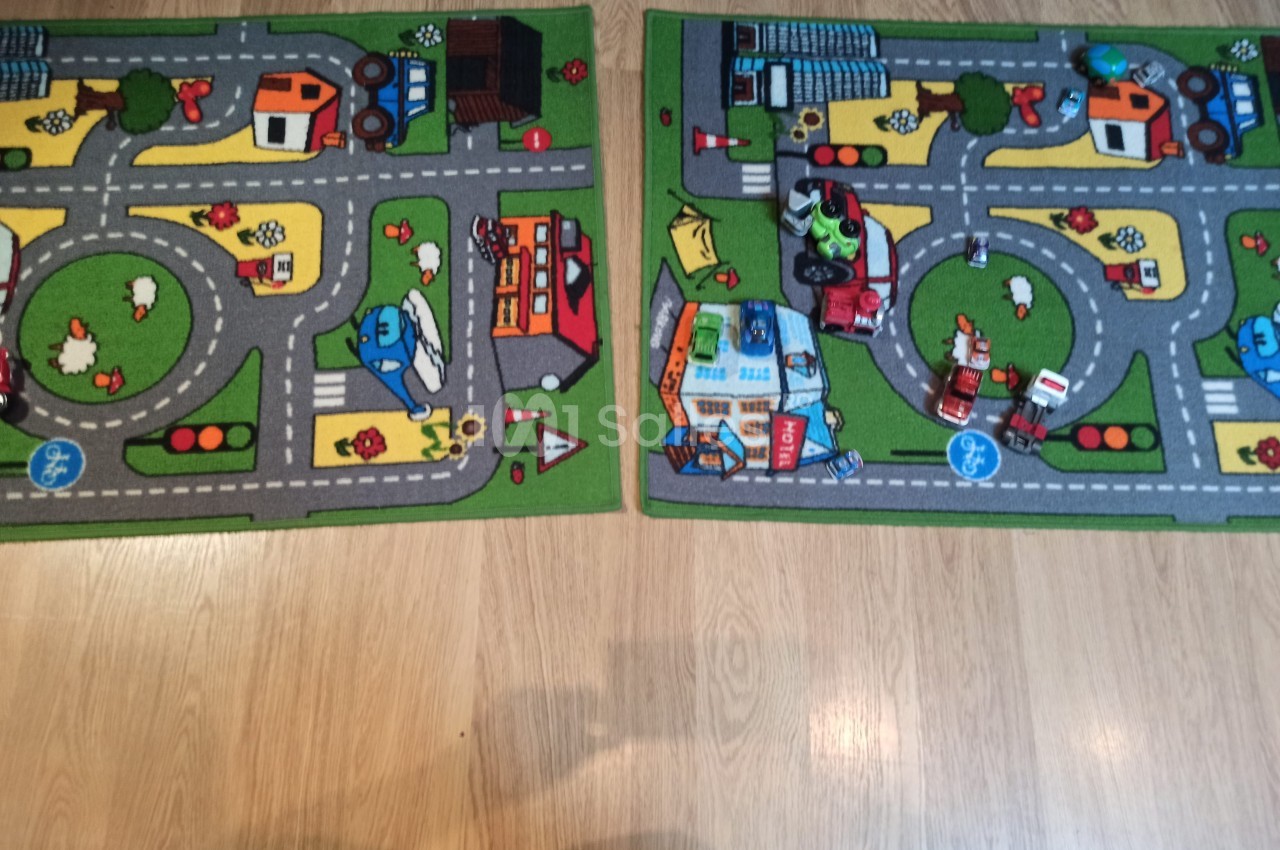 Deux tapis pour enfants avec des motifs de routes, véhicules et bâtiments, posés sur un sol en bois clair.